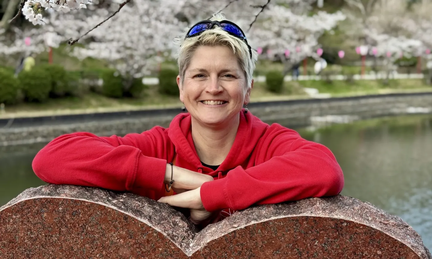 Anja Mattausch, Seniorenassistentin, lächelnd am Wasser unter blühenden Kirschbäumen