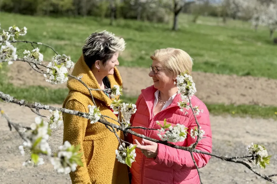 Anja Mattausch und eine Seniorin im Gespräch unter blühenden Zweigen