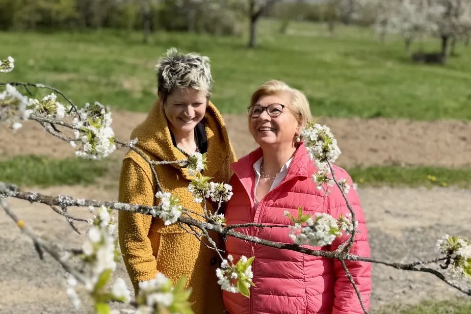 Anja Mattausch und eine Seniorin lachen unter blühenden Zweigen