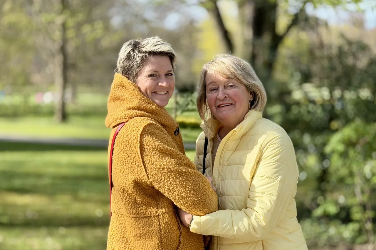 Anja Mattausch und eine Seniorin lächelnd Arm in Arm im Park